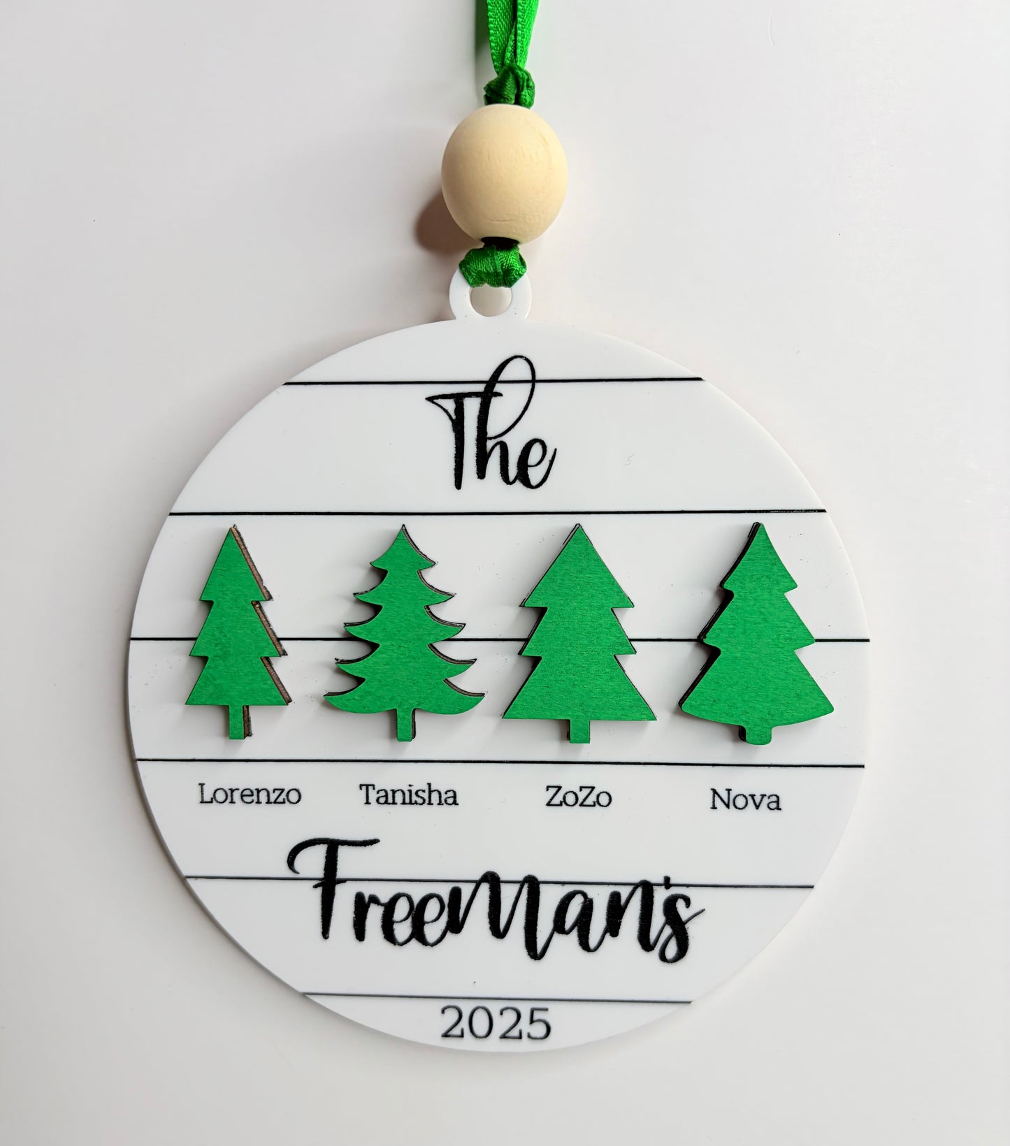 Personalized Christmas ornament with green trees and names on a white background